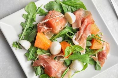 Photo of Fresh melon with prosciutto, mozzarella and arugula on light grey table, above view