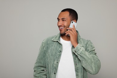 Photo of Smiling African American man talking on smartphone against light grey background. Space for text