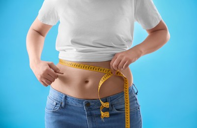 Photo of Woman with measuring tape on light blue background, closeup. Overweight problem after New Year party