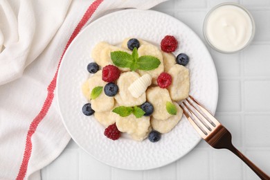 Photo of Plate of tasty lazy dumplings with berries, butter and mint leaves on white tiled table, flat lay