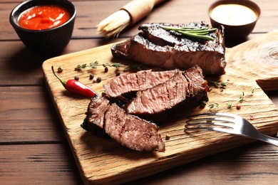 Photo of Cutting board with delicious steak served for barbecue party on wooden table