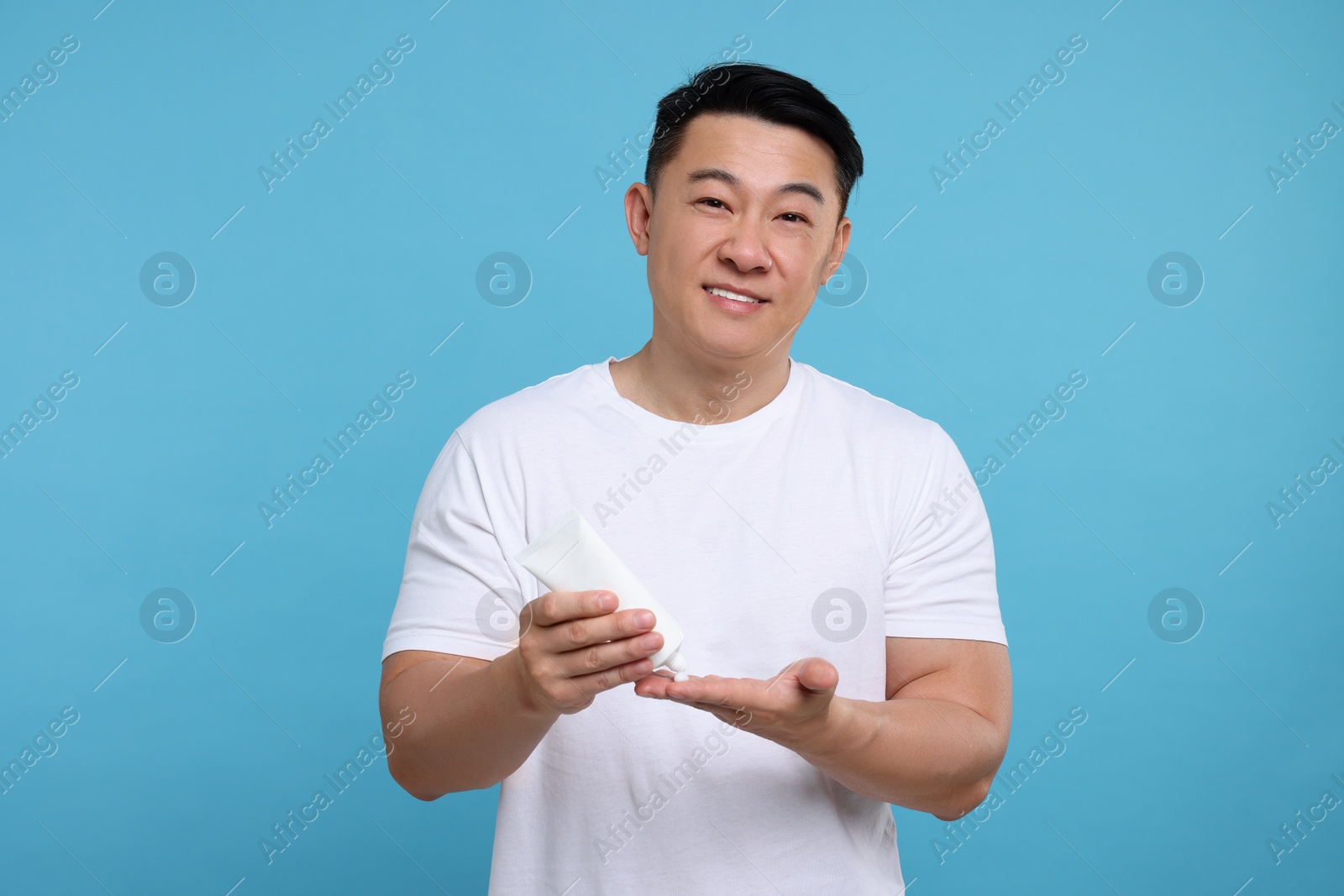 Photo of Handsome man applying body cream onto his hand on light blue background