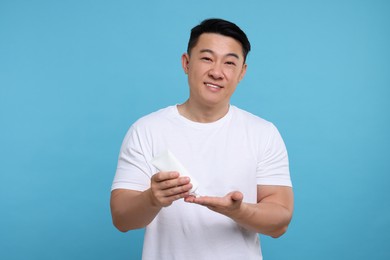 Handsome man applying body cream onto his hand on light blue background