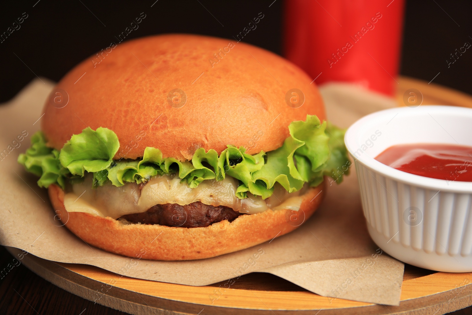 Photo of Tasty cheeseburger and sauce on wooden board, closeup