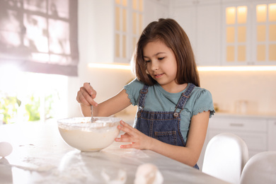 Photo of Cute little girl cooking dough in kitchen at home