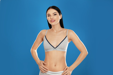 Beautiful young woman in grey sportive underwear on blue background