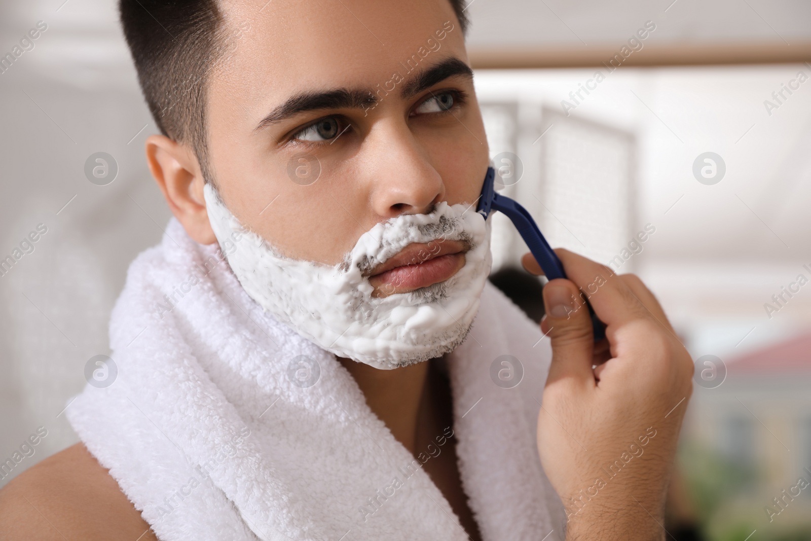 Photo of Handsome young man shaving with razor in bathroom, closeup