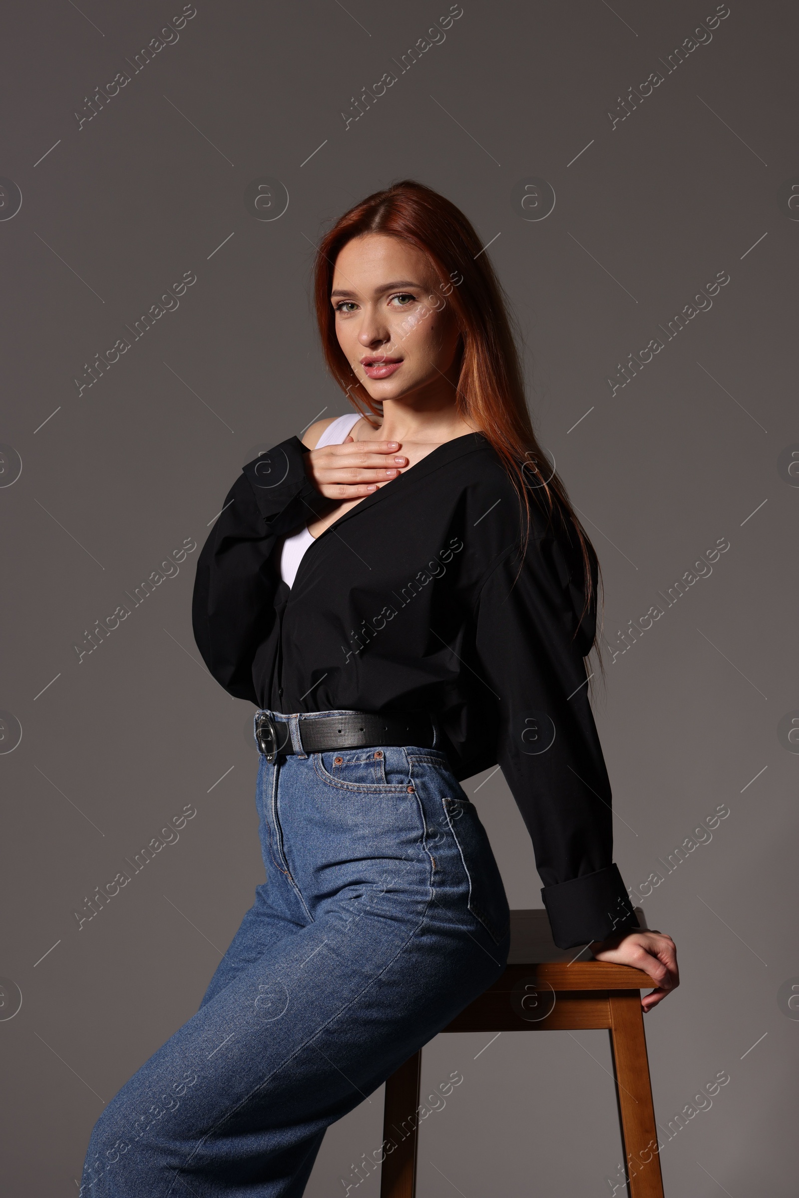 Photo of Beautiful young woman sitting on stool against gray background