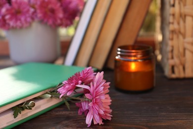 Book with beautiful chrysanthemum flowers as bookmark and candle on wooden table, closeup