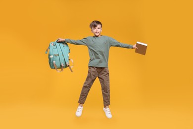 Photo of Cute schoolboy with book jumping on orange background