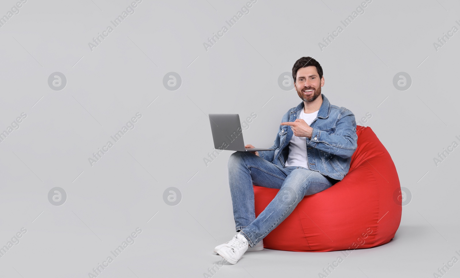 Photo of Happy man with laptop sitting on beanbag chair against light grey background