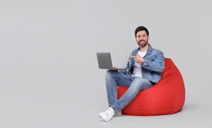 Happy man with laptop sitting on beanbag chair against light grey background