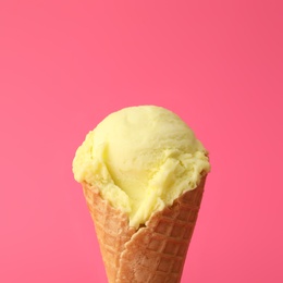 Delicious yellow ice cream in waffle cone on pink background, closeup