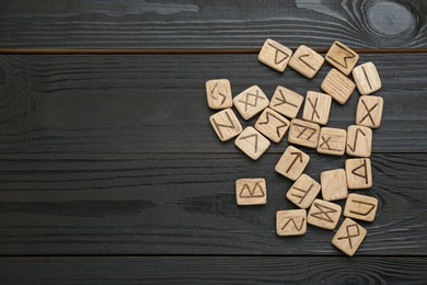 Photo of Runes with different symbols on black wooden table, flat lay. Space for text