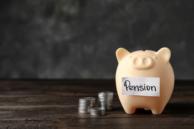 Photo of Piggy bank with word PENSION and coins on table. Space for text