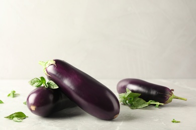Photo of Ripe eggplants and basil on light grey marble table