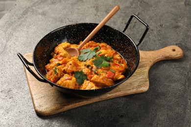 Photo of Delicious chicken curry in frying pan and spoon on grey table