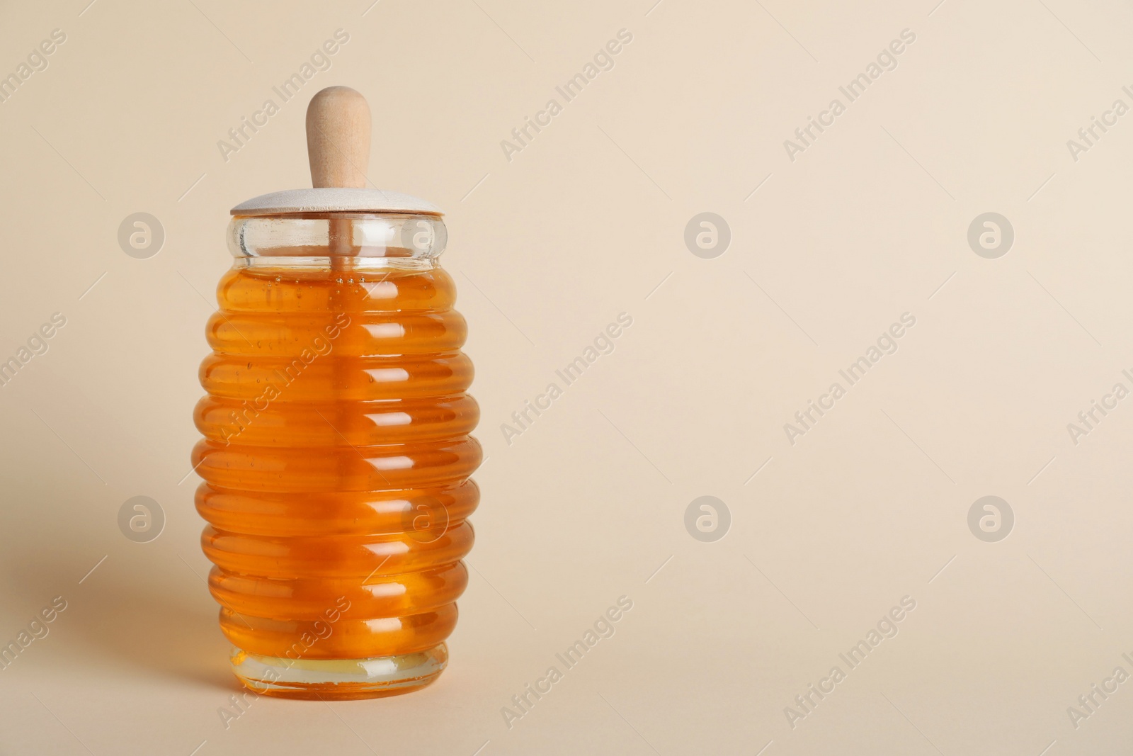 Photo of Jar of organic honey with dipper on beige background. Space for text