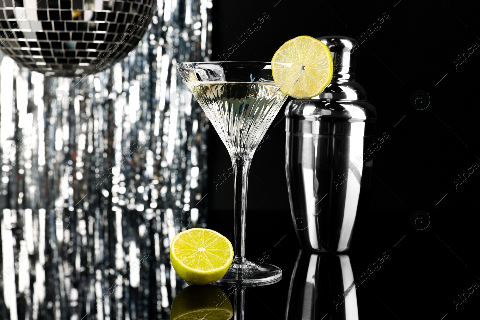 Photo of Martini cocktail with lemon slice and shaker on black and silver background