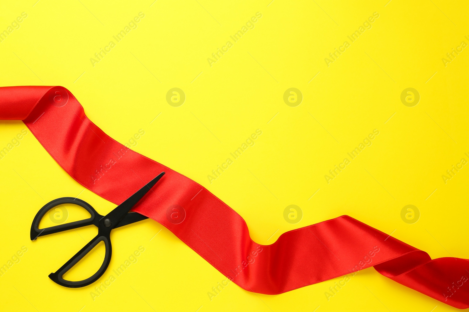 Photo of Red ribbon and scissors on yellow background, top view. Space for text