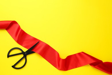 Photo of Red ribbon and scissors on yellow background, top view. Space for text