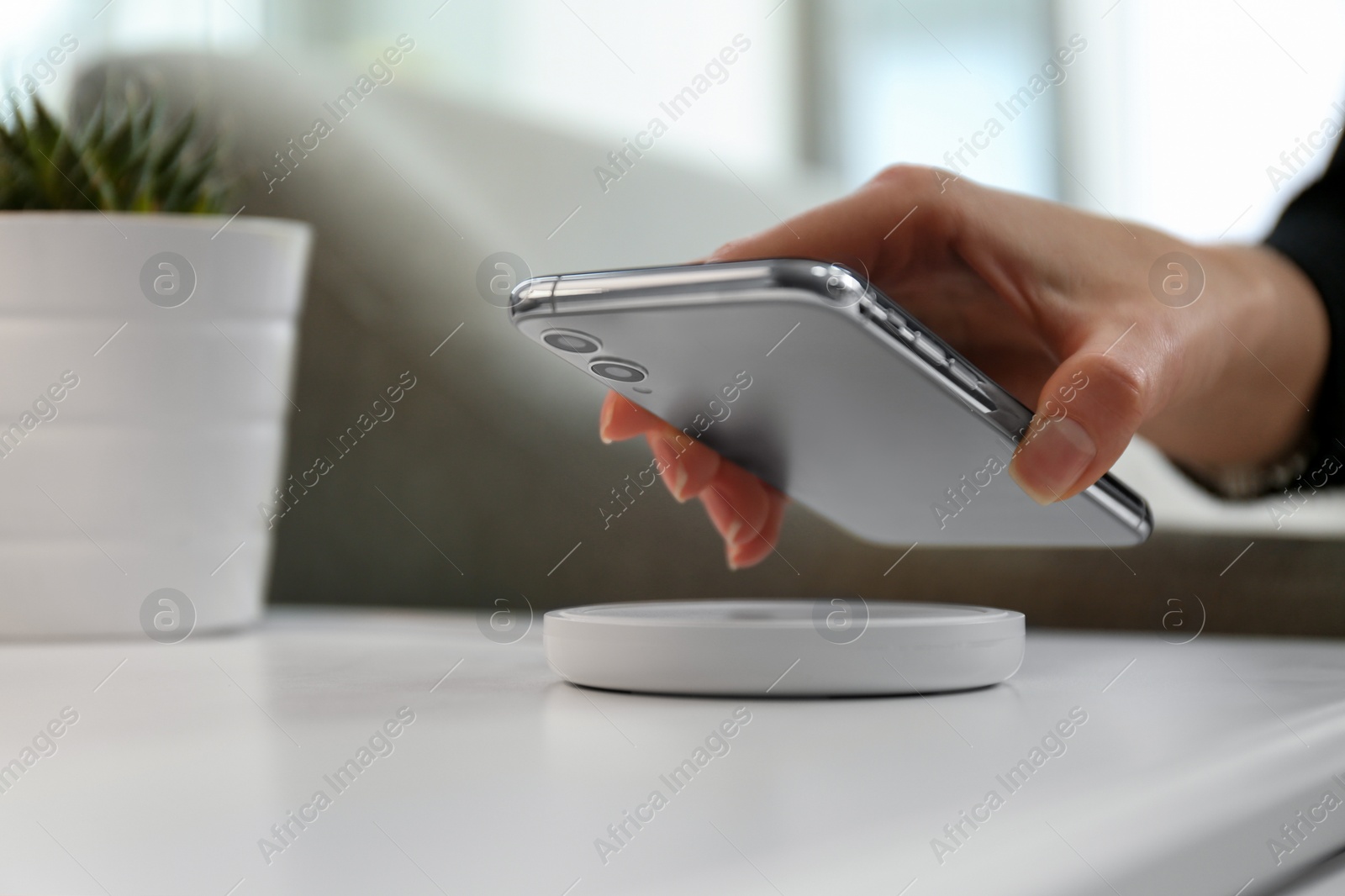 Photo of Woman putting smartphone on wireless charger in room, closeup
