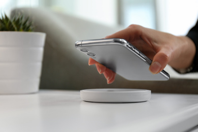 Photo of Woman putting smartphone on wireless charger in room, closeup