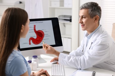 Photo of Gastroenterologist showing screen with illustration of human stomach model to patient at table in clinic