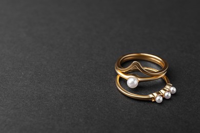 Elegant pearl rings on black background, closeup. Space for text