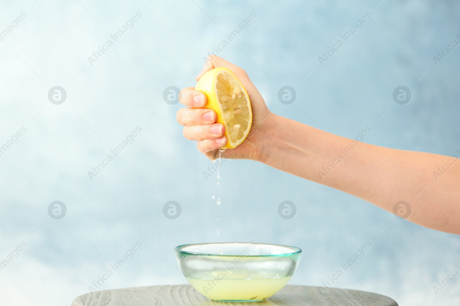 Photo of Young woman squeezing lemon juice into bowl on color background