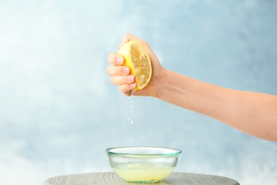 Photo of Young woman squeezing lemon juice into bowl on color background