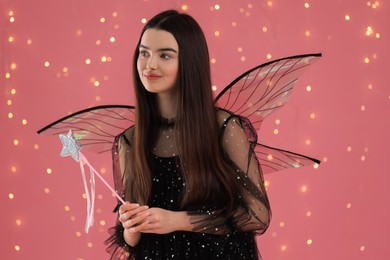 Photo of Beautiful girl in fairy costume with wings and magic wand on pink background