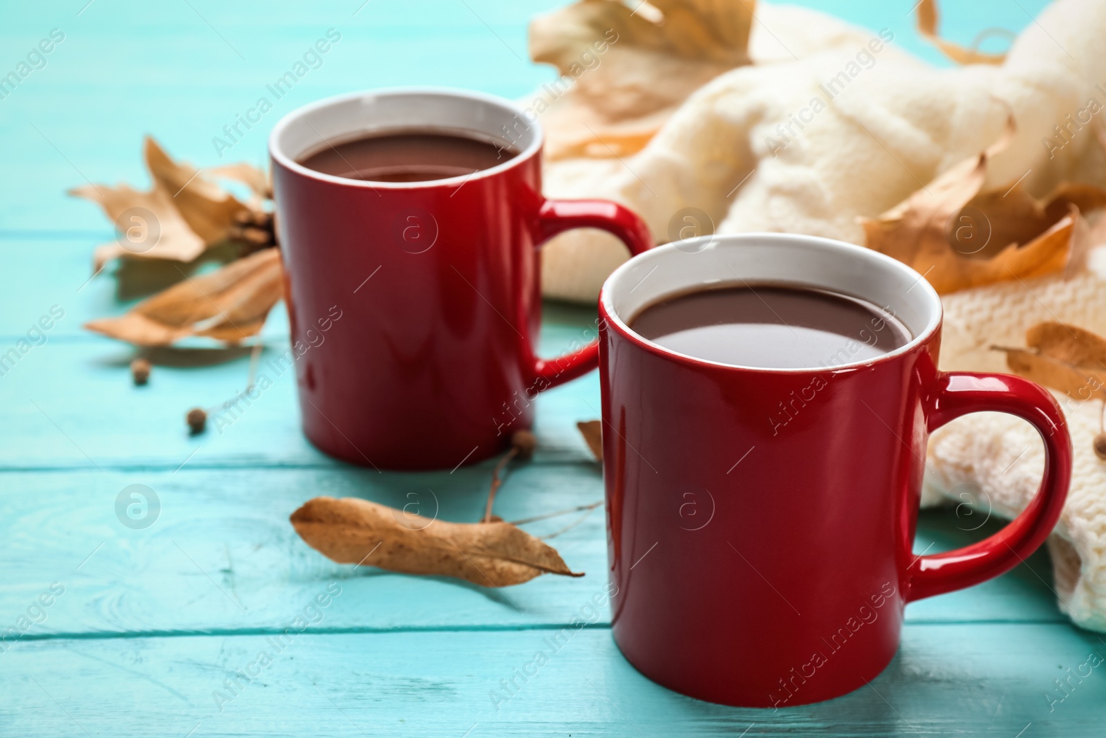 Photo of Cups of hot drink and knitted sweater on blue wooden table. Cozy autumn atmosphere