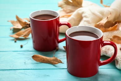 Photo of Cups of hot drink and knitted sweater on blue wooden table. Cozy autumn atmosphere