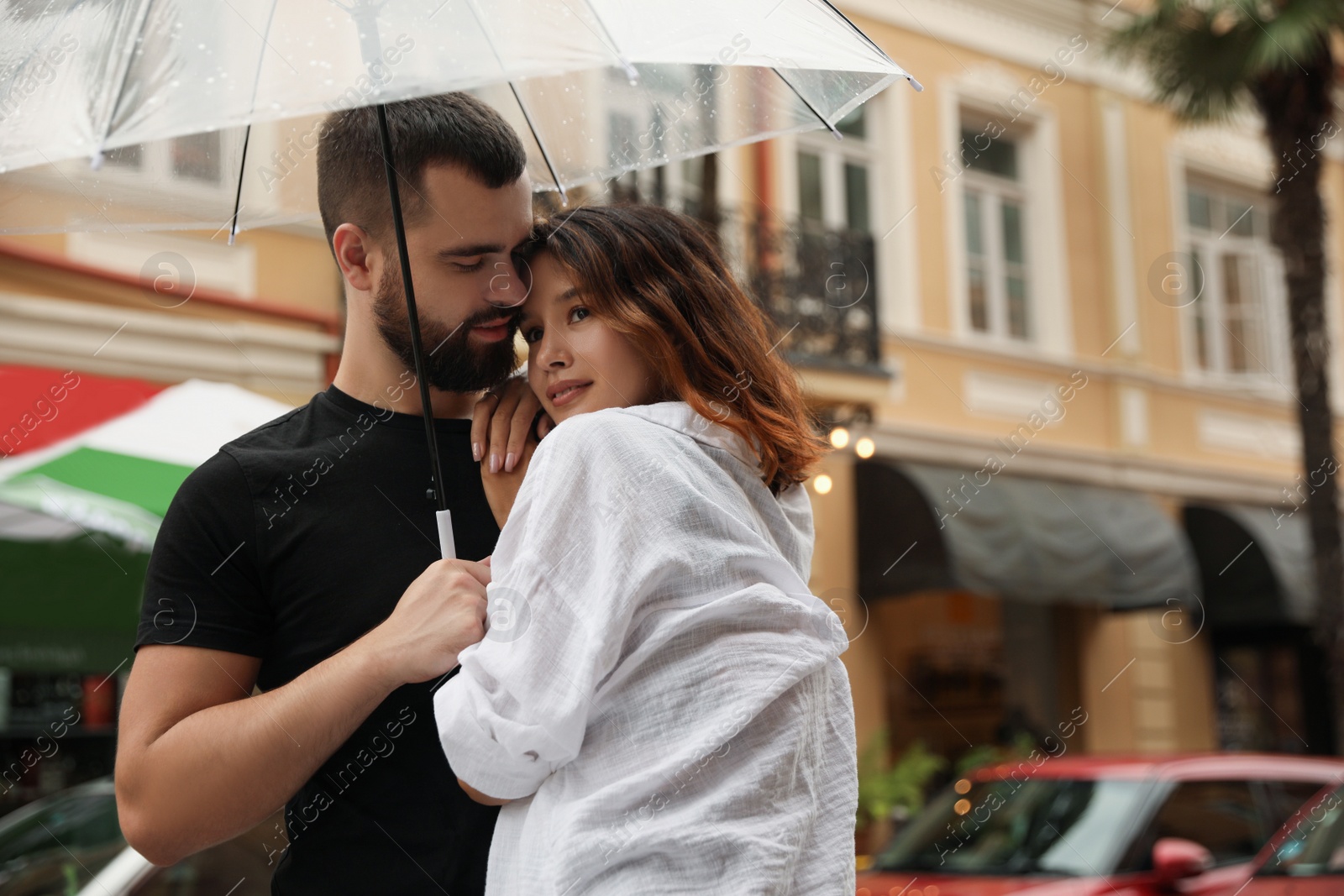 Photo of Young couple with umbrella enjoying time together under rain on city street