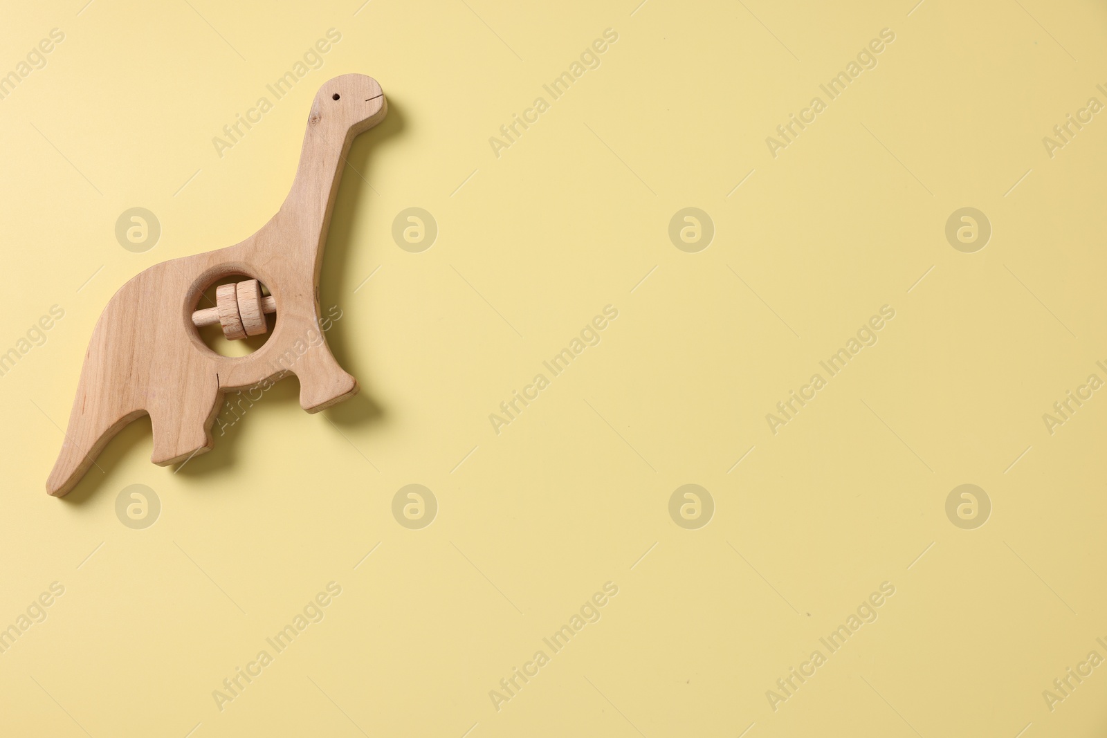Photo of Baby accessory. Wooden rattle on yellow background, top view. Space for text