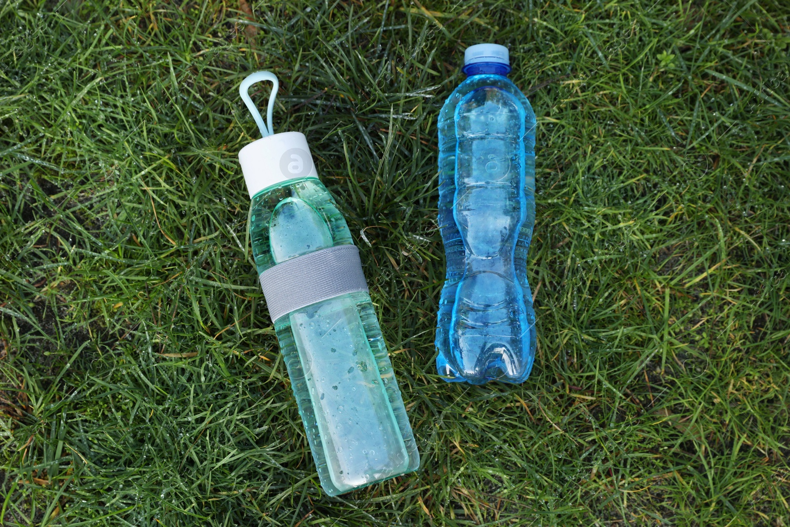 Photo of Bottles of fresh water on green grass outdoors, flat lay