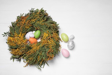 Festively decorated Easter eggs and nest of beautiful spring flowers on white wooden table, flat lay. Space for text