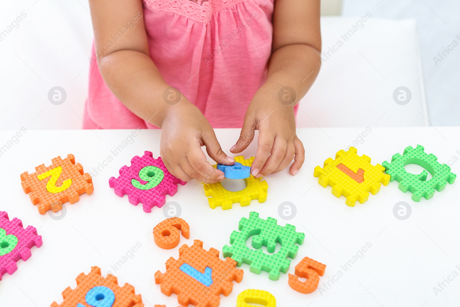 Photo of Little girl playing with colorful puzzles at white table, closeup. Educational toy