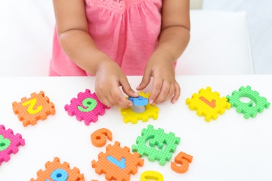 Little girl playing with colorful puzzles at white table, closeup. Educational toy