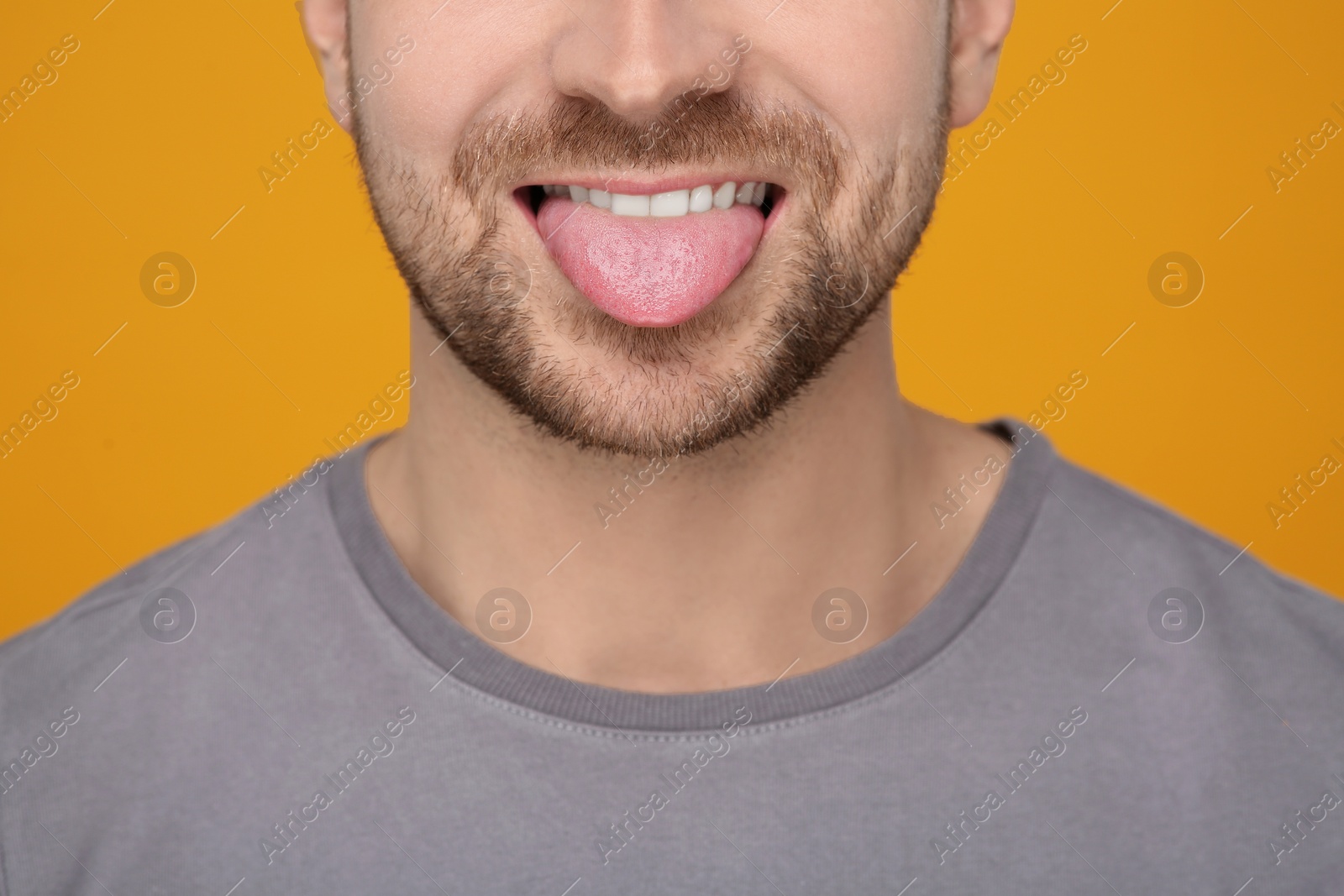 Photo of Man showing his tongue on orange background, closeup