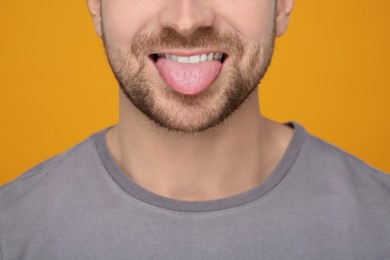 Man showing his tongue on orange background, closeup
