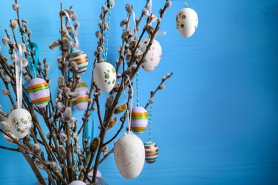 Photo of Closeup view of beautiful willow branches with painted eggs on light blue wooden background, space for text. Easter decor