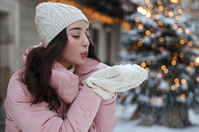Photo of Portrait of beautiful woman blowing snow from hands outdoors in winter