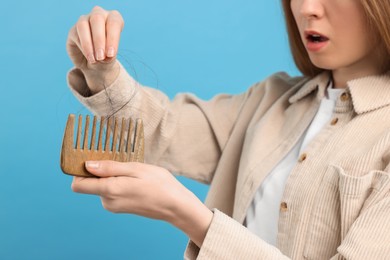 Photo of Woman untangling her lost hair from comb on light blue background, closeup. Alopecia problem