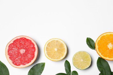 Photo of Different cut citrus fruits and leaves on white table, flat lay. Space for text