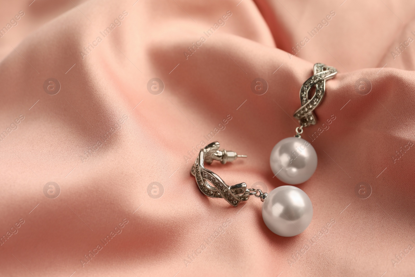 Photo of Elegant silver earrings with pearls on pink silk, closeup