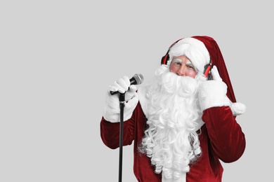 Photo of Santa Claus with headphones and microphone on light grey background, space for text. Christmas music
