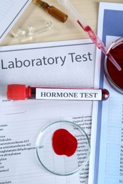 Hormone test. Sample tube with blood and laboratory form on table, flat lay