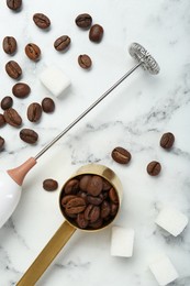 Photo of Milk frother wand, sugar cubes and coffee beans on white marble table, flat lay